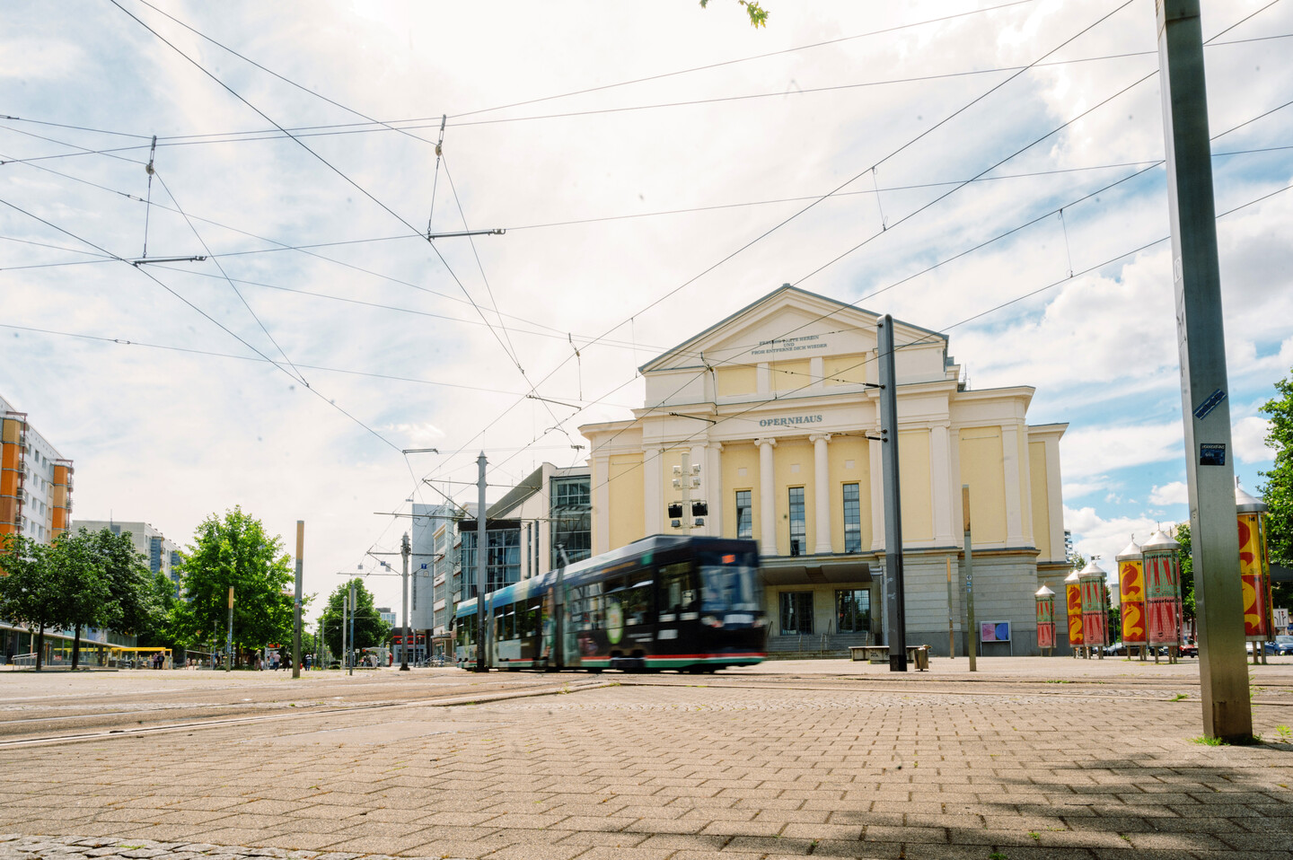 Außenbild des Magdeburger Opernhauses. Vor dem gelb-weißen klassizistischen Gebäude fährt eine Straßenbahn