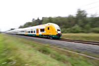 Ein weiß-grün-gelber Zug der ODEG fährt schnell durch die Landschaft