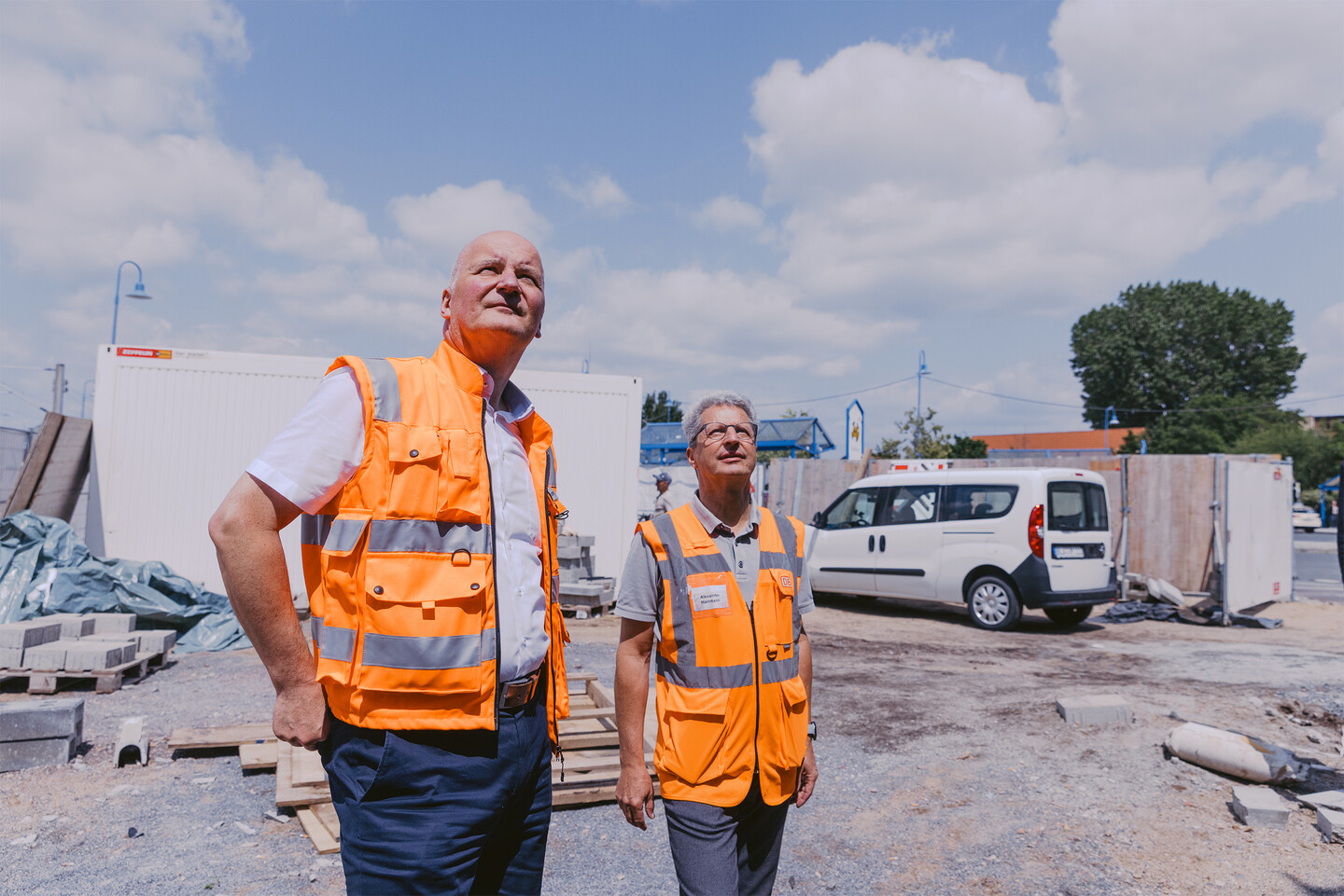 Zwei Männer in orangen Warnwesten (Kasten Kammler und Alexander Hartmann) stehen auf der Bahnhofsbaustelle.