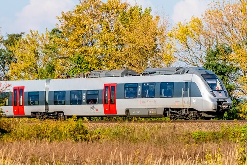 Ein silber-roter Zug des Typs Bombardier Talent 2 von DB Regio fährt durch eine herbstliche Landschaft