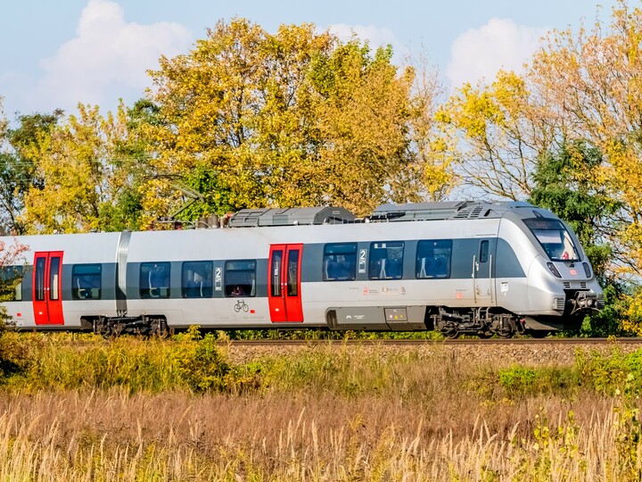 Ein silber-roter Zug des Typs Bombardier Talent 2 von DB Regio fährt durch eine herbstliche Landschaft