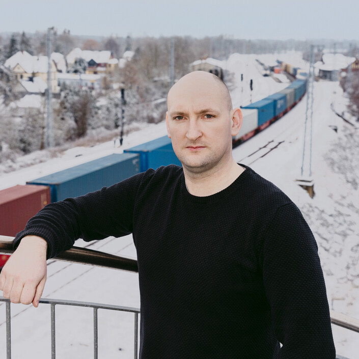 Ein Mann Steht auf einer Treppe, im Hintergund ist ein Güterzug im Schnee zu sehen.