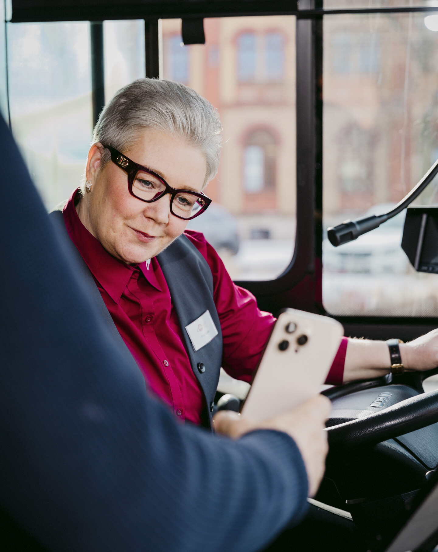 Eine Busfahrerin in rot-schwarzer Uniform kontrolliert ein Ticket auf einem Handy.