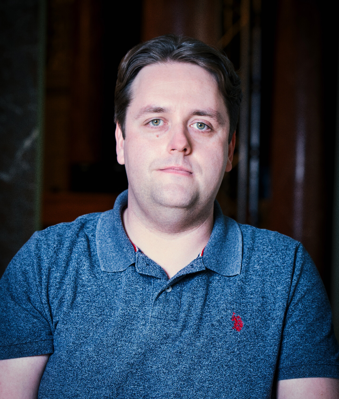 Portrait von Sascha Krebs. Der Mann im dunkelblauen Polo schaut in die Kamera hinter ihm ist eine Bühne zu sehen.