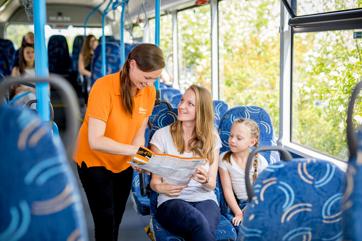 Eine Mitarbeiterin des Mobilteams hilft einem Fahrgast im Bus beim Lesen des Taschenfahrplans.