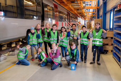 Kinder mit grünen Warnwesten in einer Eisenbahnhalle.