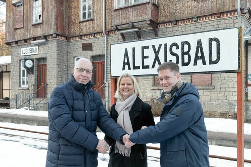 Zwei Männer und eine Frau (Markus Hercher, HSB-Geschäftsführerin Katrin Müller und Harzgerodes Bürgermeister Marcus Weise) geben sic vor einem Bahnhoffschild mit der Auschrift "Alexisbad" die Hand
