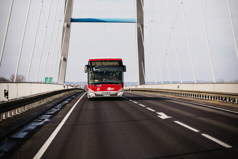 Ein roter Bus mit der Zielanzeige „34SEV Rethenow“ fährt über eine Brücke auf uns zu.