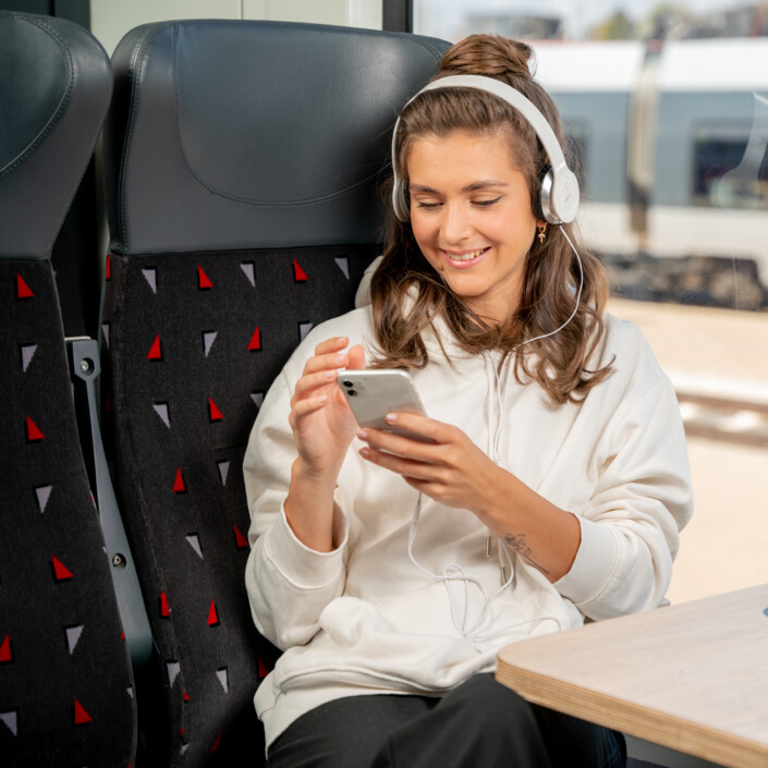 A young woman sits on the train and happily looks at her cell phone.