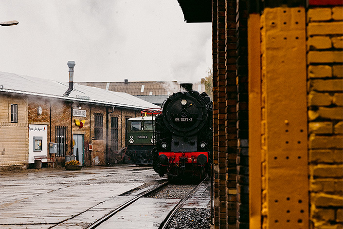 Blick auf die Front einer Dampflokomotive, auf der rechten Seite ist eine Mauer im Vordergrund